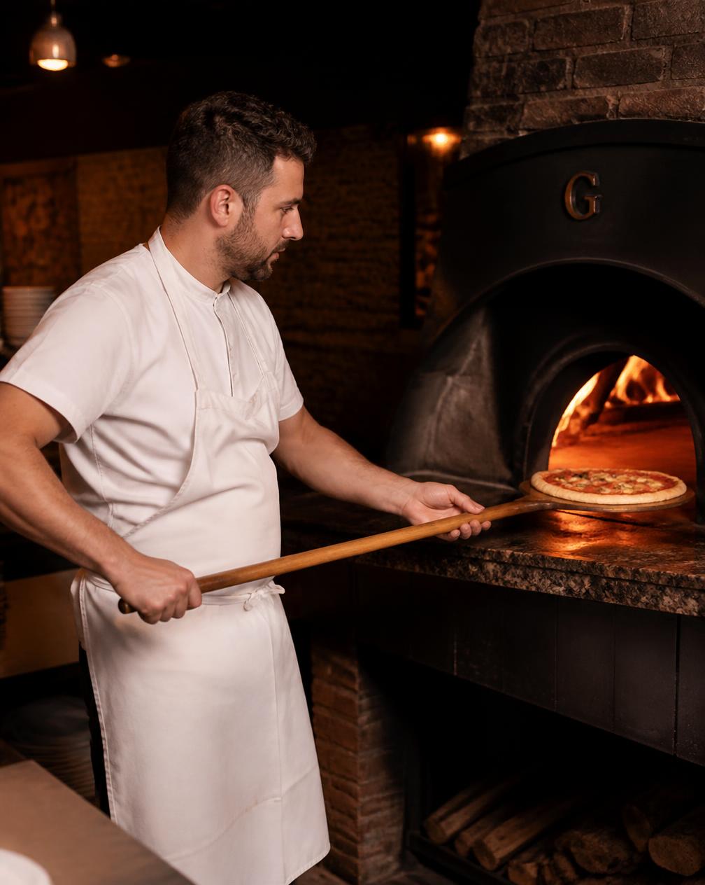 Pizzabäcker schiebt eine Pizza in den Holzofen